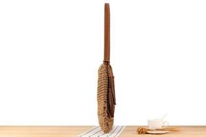 Close-up of khaki woven straw bag with dark brown leather strap and side tassel detail