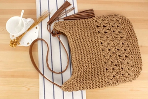 Detail of hand-woven straw tote bag featuring hollow patterns and brown tassel charms