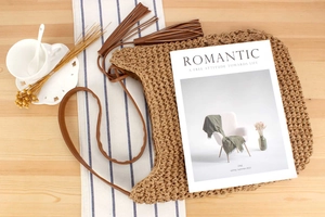 Detail of a brown woven crescent bag with leather straps and tassels on a beach setup