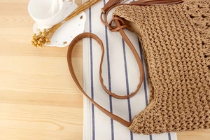 Close-up of woven straw texture and brown leather strap on a vintage summer tote bag