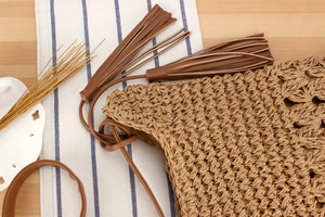 Close-up of woven straw texture and decorative brown leather tassels on a vacation handbag