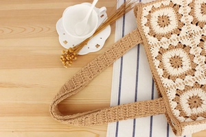 Detail of handmade crochet floral tote bag on wooden table with elegant lifestyle props
