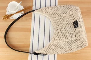 Close-up of cream hollow woven bag with black leather strap and adjustable buckle