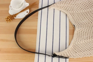 Detail of hand-woven cream crochet bag featuring slim black leather strap with metal buckle