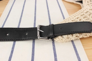 Close-up of black leather belt with silver square buckle on beige crochet beach bag