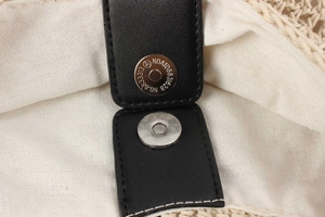 Detail of silver magnetic buckle on black lychee leather strap with woven texture