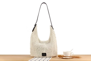 Detail view of a cream crochet hobo bag with a dark leather strap on a wooden table