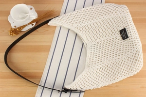 Macro view of white crochet mesh shoulder bag with black leather strap and brand label
