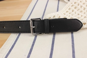 Close-up of black leather belt with silver buckle on blue striped textile background