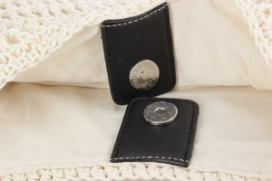 Detailed macro view of the metal magnetic clasp and black leather trim on a woven bag
