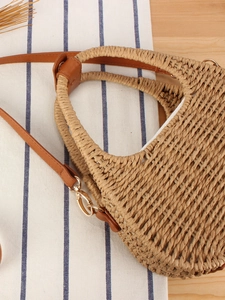 Borsa in paglia intrecciata a mano con telaio in metallo e tracolla su sfondo rustico