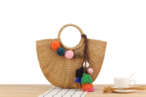 Detail of handmade straw bag with colorful pom-poms and tassels on a wooden surface