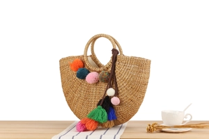 Detail of handmade straw tote featuring colorful pom-poms and long tassels on wooden table