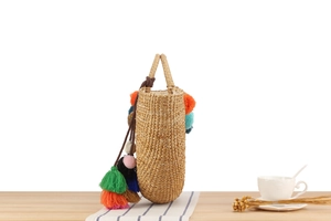 Detail of hand-woven straw bucket bag with colorful pompom tassels and natural texture