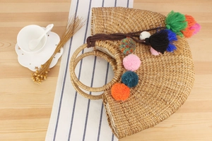 Close-up of handmade straw tote bag with colorful pom-poms and tassels on wood table