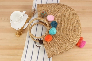 Detail of handmade straw bag with vibrant colorful pom poms and decorative tassels