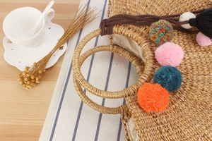 Detail of straw woven bag with colorful pom-poms and round rattan handles on wooden table