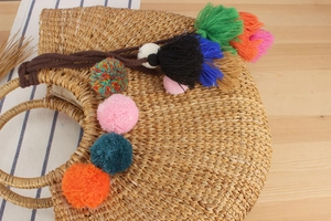 Detail of handmade straw bag with colorful pom-poms and integrated round woven handles