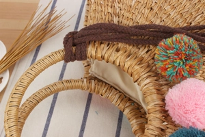 Close-up of handmade straw tote with colorful pompoms and thick woven handles