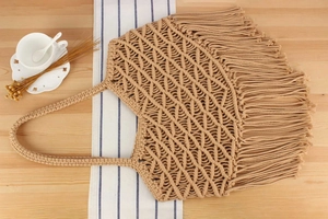 Detail of bohemian cotton rope woven handbag with long tassels on a rustic wooden table