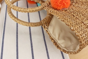 Close-up of handmade straw tote with colorful pom-poms and beige cotton lining details