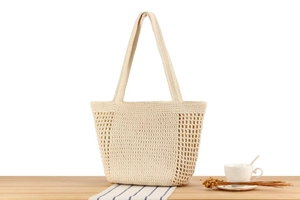 Detail of a beige hollow-out woven tote bag on a wooden table with rustic home decor