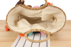 Detail view of woven straw tote bag with colorful pom-pom trim and canvas lining