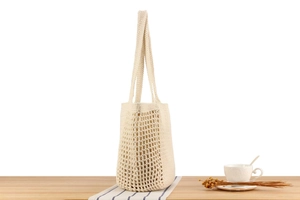 Detail of cream woven cotton rope bag showing hollow mesh texture on a wood table