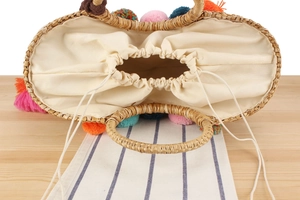 Top view of straw tote bag with colorful pom-poms and white canvas drawstring liner