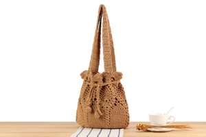 Handwoven straw bucket bag with drawstring closure and wide strap on wooden desk