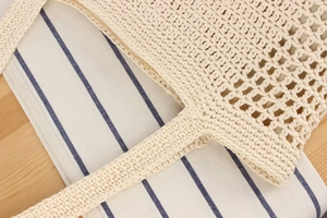 Macro detail of hand-woven off-white hollow knit tote bag on a rustic wooden table