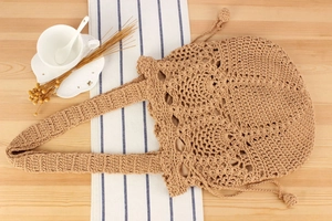 Close-up of beige handmade crochet tote bag with hollow pattern on a wooden surface