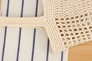 Detailed close-up of handmade hollow woven texture on a beige straw crochet tote bag