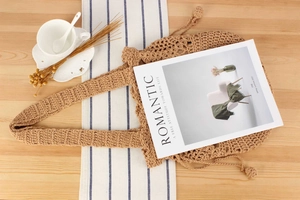 Detail of handmade crochet tote bag with wavy edges and tassel on a rustic wooden table