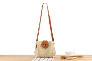 Detail of hand-woven straw crossbody bag with leather trim and gold bee buckle