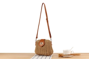 Detail of hand-woven straw crossbody bag with brown leather flap and golden buckle