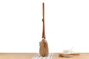 Detail view of woven straw crossbody bag with brown leather strap on lifestyle background
