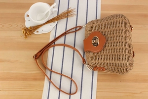 Detail of hand-woven straw crossbody bag with golden bear-shaped lock on wood surface