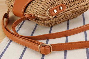 Close-up of handmade straw crossbody bag showing tan leather trim and gold metal hardware