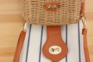 Macro detail of hand-woven straw bag featuring metallic bow buckle and rhinestone