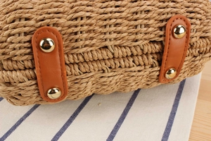 Detail of woven straw bag bottom with brown leather straps and gold metal rivets
