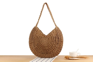 Detail view of the intricate hollow weave pattern on a brown straw shoulder bag