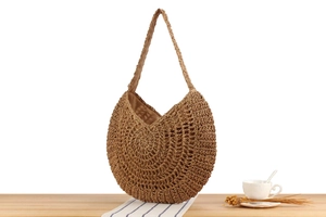 Detail of hand-woven straw shoulder bag with hollow mesh pattern on wooden table