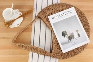 Detail of handmade woven straw bag on wooden table with magazine and coffee cup
