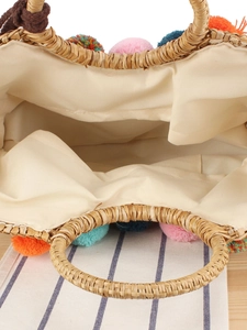 Handwoven straw tote bag with colorful pom poms and round top handles for summer vacation