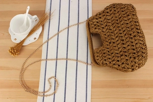 Borsa a mano in paglia marrone con catena dorata su un tavolo in legno rustico