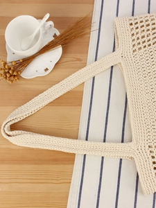 Chic cream handmade crochet woven handbag with top handle on a wooden table setup
