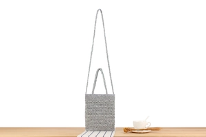 Detail of silver crochet crossbody bag with textured weave on a wooden table setup