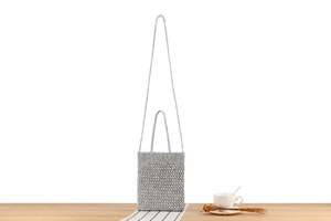 Detail view of silver crochet handbag with metallic chain strap on wooden table