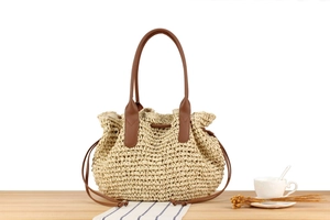 Detail der beigen Strohtasche mit braunen Ledergriffen und Kordelzugverschluss